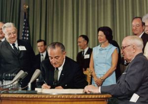 President Lyndon B. Johnson signing the Medicare bill at the Harry S. Truman Library in Independence, Missouri. Former President Harry S. Truman is seated at the table with Johnson. In the background (from left to right) are Sen. Edward V. Long, an unidentified man, Sen. Mike Mansfield, Lady Bird Johnson, Vice President Hubert Humphrey and Bess Truman. CREDIT EXECUTIVE OFFICE OF THE PRESIDENT OF THE UNITED STATES