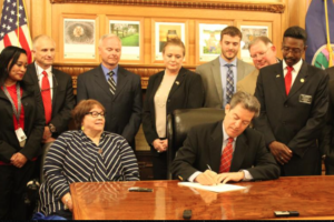 Photo by Megan Hart/KHI News Service Gov. Sam Brownback signs Senate Bill 402, which includes new restrictions on public assistance, Monday at the Statehouse. Seated at left is Phyllis Gilmore, secretary of the Kansas Department for Children and Families.