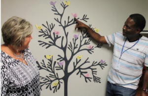 Photo by Wyandot Center Kristen Whitney, left, service coordinator for the Cooperative Agreements to Benefit Homeless Individuals grant at Wyandot Center, and Michael DePriest, a case manager, explain a visual representation of chronically homeless people who have gained housing through their programs since January. Each bird has the initials of a Wyandot Center client who now has housing. 